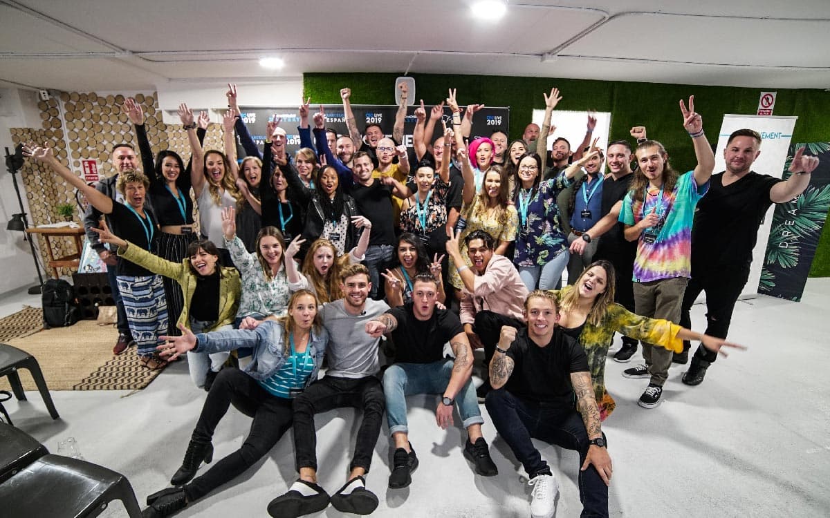 A large group of attendees, arms up, in a group photo after a session