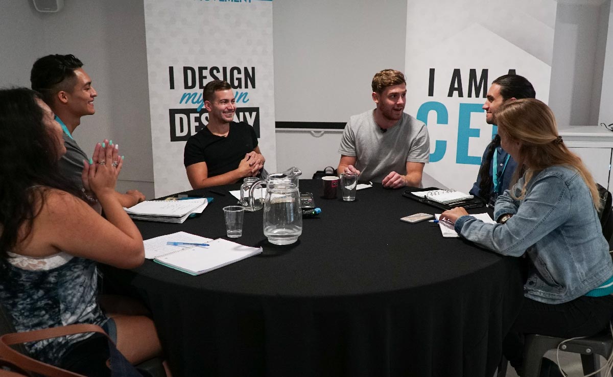 A working roundtable, notebooks open, in front of an 'I am a CEO' banner